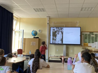 Die Schüler sehen ein Schwarz-Weiss-Foto aus der Zeit, in der die Geschichte spielt. Es ist eine Lehrerin mit ihren Schülern zu sehen.